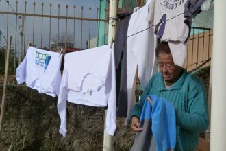 Dona Maria aproveita o sol para secar a roupa e se aquecer enquanto espera