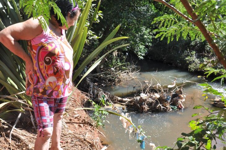 Moradora observa a cerca de arame que antes ficava quase dois metros de distância da água